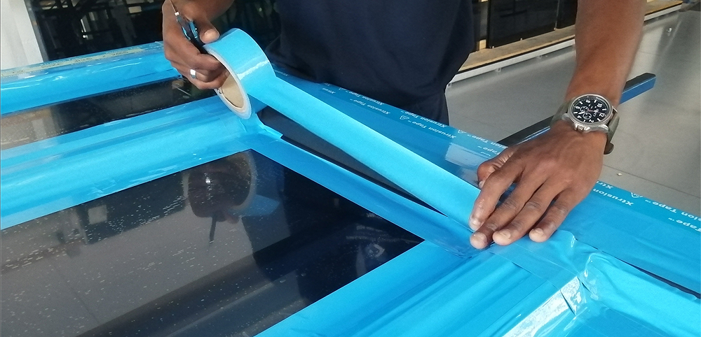 Technician applying Premium Blue Protective Tape to an aluminium window frame.